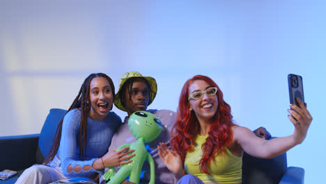 Studio-Shot-Of-Group-Of-Gen-Z-Friends-Sitting-On-Sofa-Posing-For-Selfie-With-Toy-Alien-On-Mobile-Phone-1